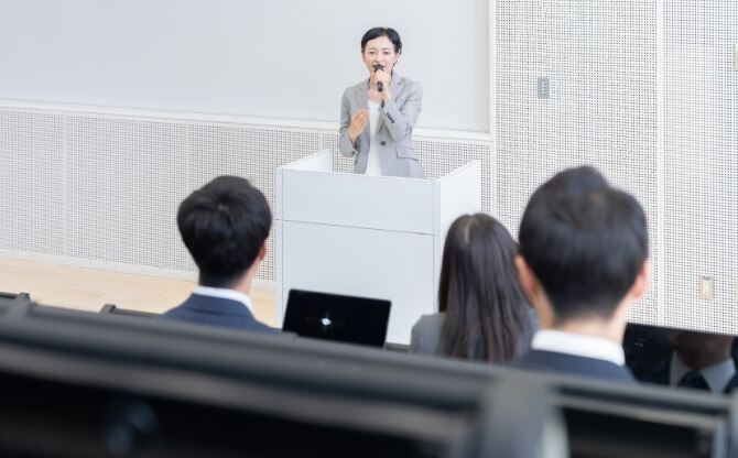 専門学校の講義室で学生に企業説明を行う女性講師