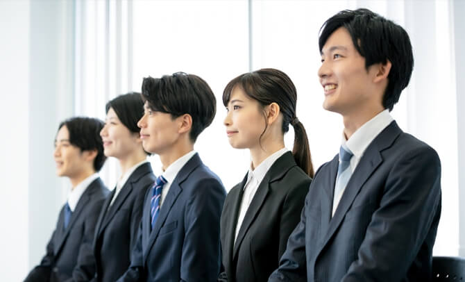 全国100校以上の有力専門学校と連携し、深度ある母集団形成を実現する採用活動。スーツ姿の学生たちが前向きな表情で並ぶ様子。